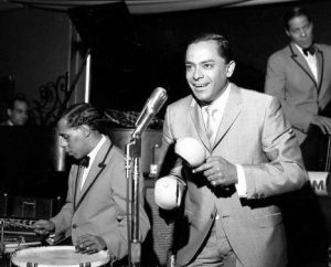 Tito Rodriguez playing maracas in front of a microphone.